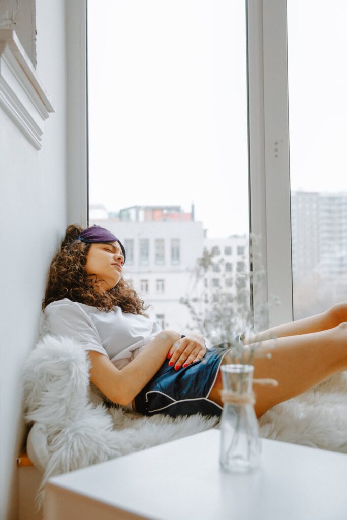 15 Thoughts Women Have On Their periods - stock photo from pexels of a woman laying down by a window with brown hair, a white t-shirt and blue shorts by Polina Zimmerman