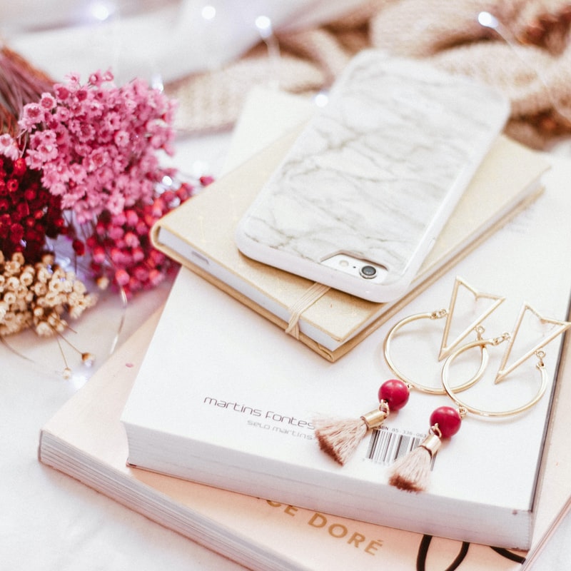 Stock image close up photo of a phone and some nooks on a table with pink flowers in the background