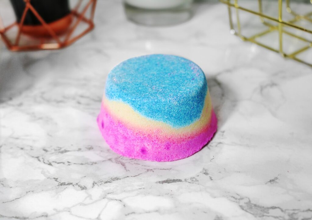 Miss Patisserie Unicorn Hoof Close up photo of the Miss Patisserie Unicorn Hoof sitting on a white marble table top. The bath bomb in pink, yellow and blue with a flat back