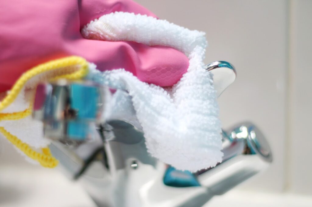 Close up of a person cleaning a silver faucet wearing pink rubber gloves and using a white cloth