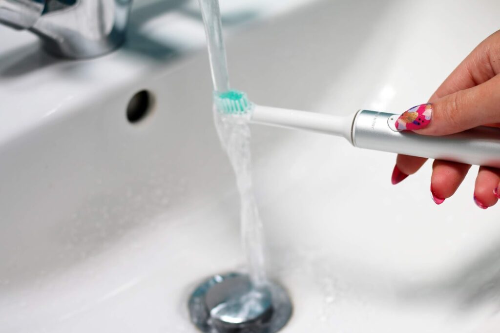 Uber sonic club silver toothbrush with water running in sink