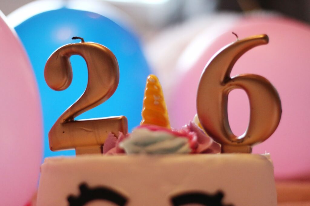Photo of the number 26 in candles on top of a white and pink unicorn cake