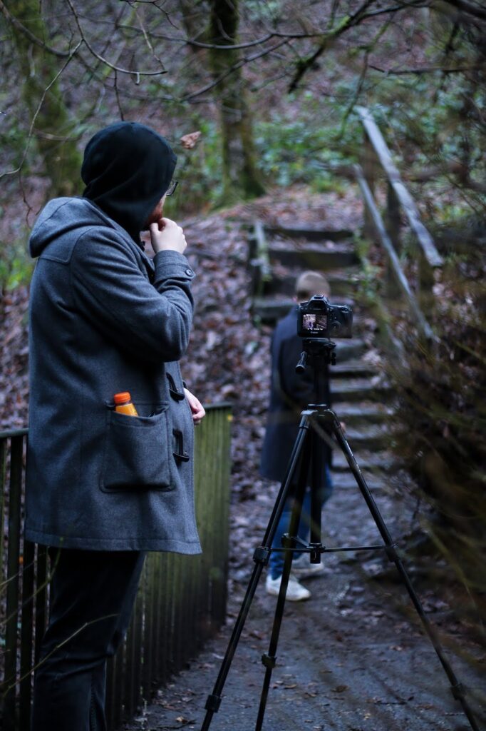 on set of analogue truths two men standing, one behind a camera filming the other walk down some stairs in Cumberland glen