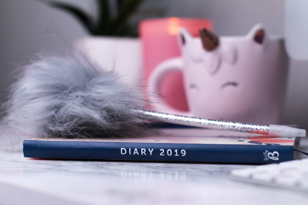 thelifeofaglasgowgirl February to do list post photo a busyb 2019 diary on a marble counter top with a grey fluffy pen on top of it. There is a white unicorn light in the background and a pink candle.