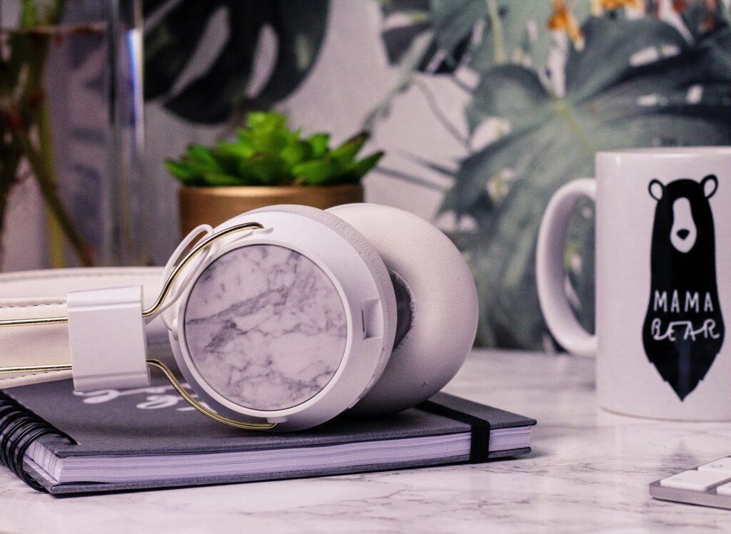 Feel good playlist - Spotify playlist to lift your mood and spirits. Songs guaranteed to lift your mood on Thelifeofaglasgowgirl.co.uk Extream Close up of white sudio headphones on a white marble desk with a white mug next to them and flowers in the background