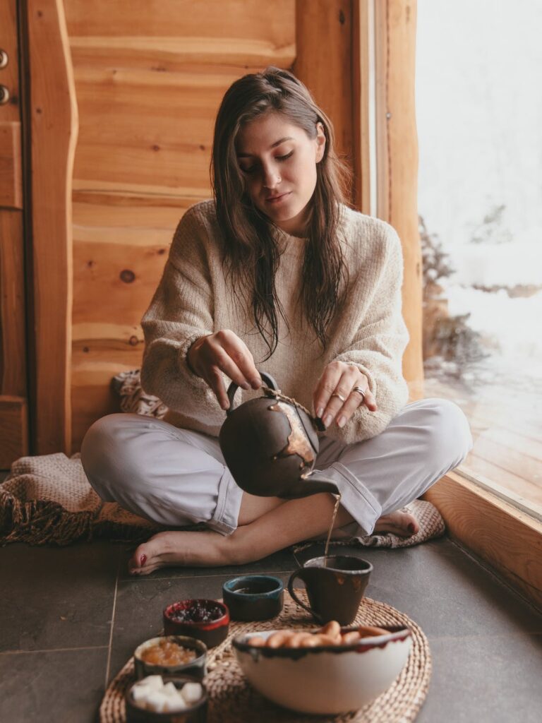 Taking Care of Yourself - Stock photo from pexels by Yaroslav Shuraev of a woman with brown hair, beige jumper and light jeans pouring tea into a mug