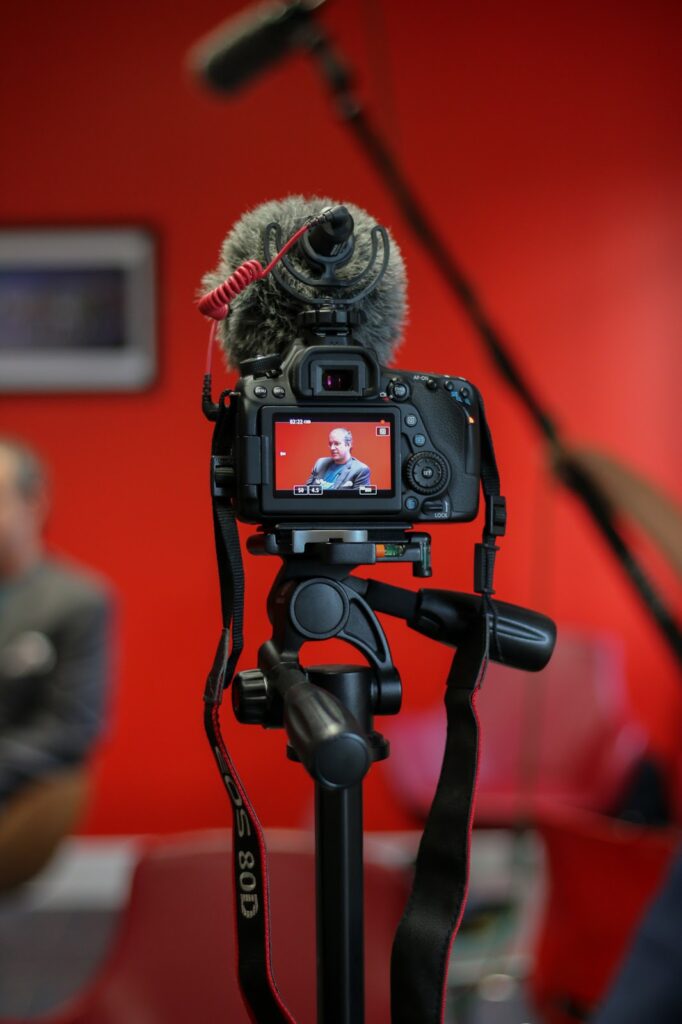 BILT Summit 2019 interview Close up photo of a black canon DSLR on a tripod as it is focused on a man being interviewed. The background is blurred with a bright red wall.