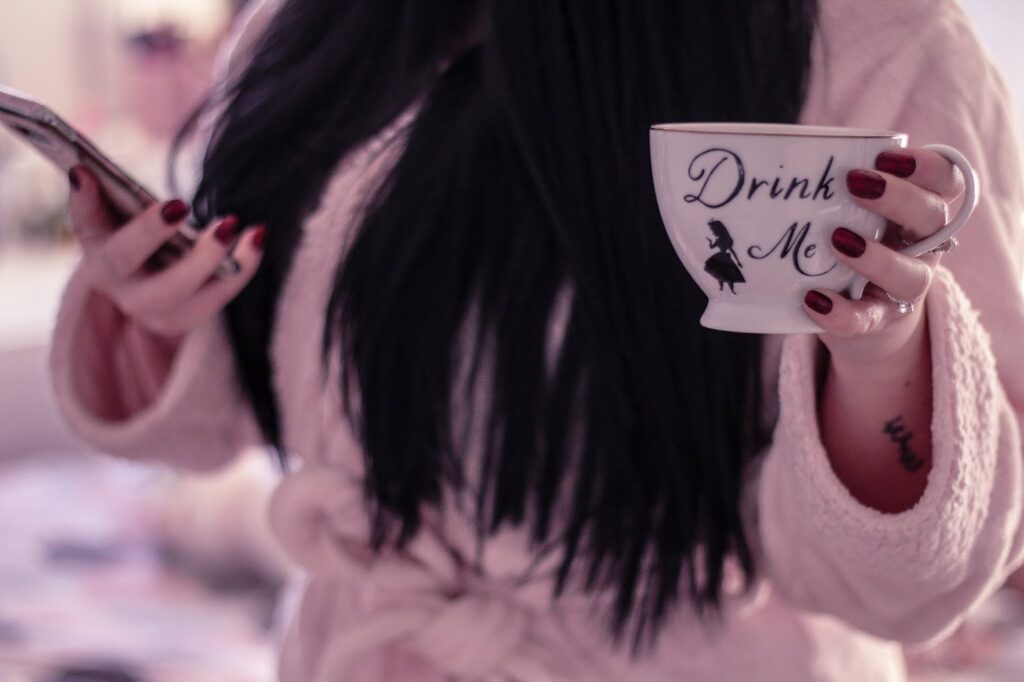 A look back at 2019 main blog photo on thelifeofaglasgowgirl.co.uk A mid shot of myself (Jordanne Lee) standing holding a phone in right hand and white tea cup with "Drink Me" written on it. I am wearing a pink robe and the background is blurred