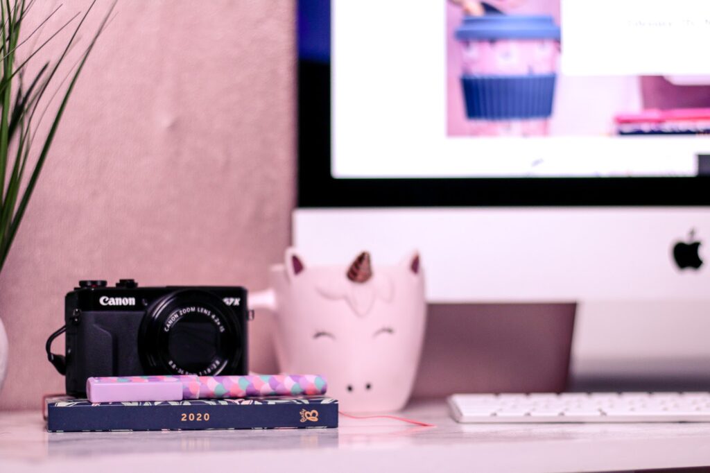 Close up photo of a computer desk with a pink unicorn mug, busy b yearly diary and a canon camera taken by ofaglasgowgirl