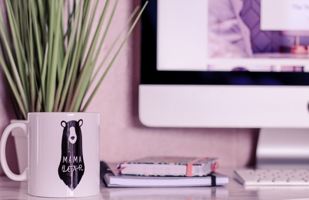 Close up of a white mug on a desk with a green plant in the background taken by ofaglasgowgirl