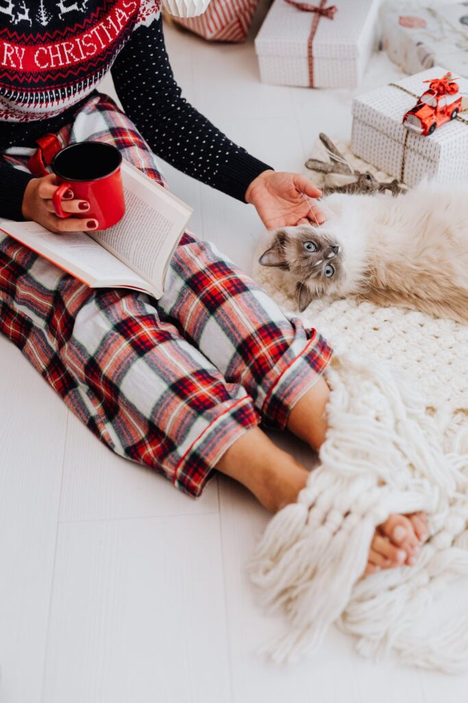 Stock photo from pexels by Karolina Grabowska of a cat laying on a white floor with a woman in plaid pyjamas petting it's head