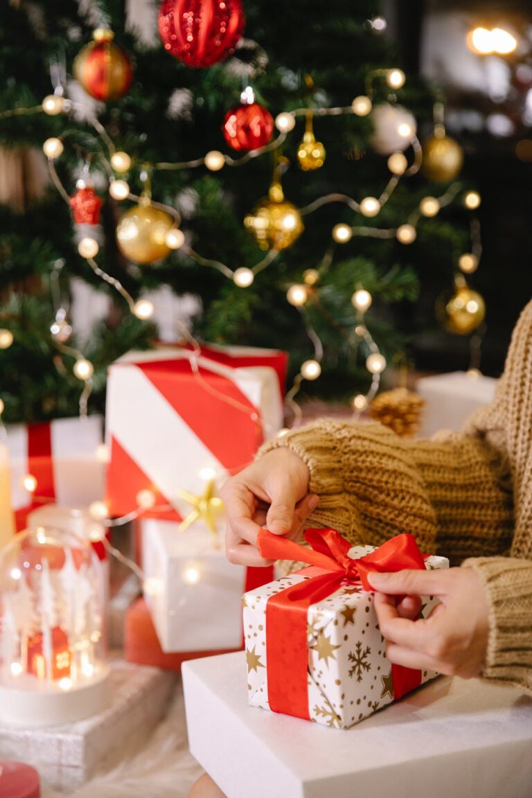 Stock photo from pexels by Laura James of a woman opening a white wrapped christmas present by a christmas tree