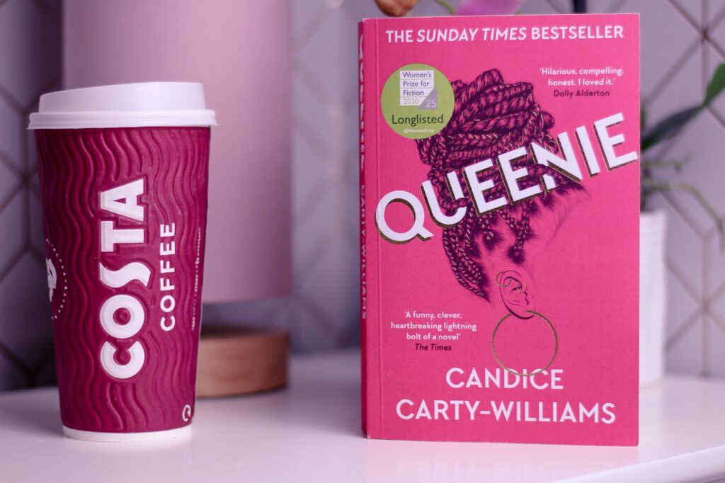 Close up photo of the book Queenie by Candice Carty-Williams on a white bedside table next to a Costa take away cup