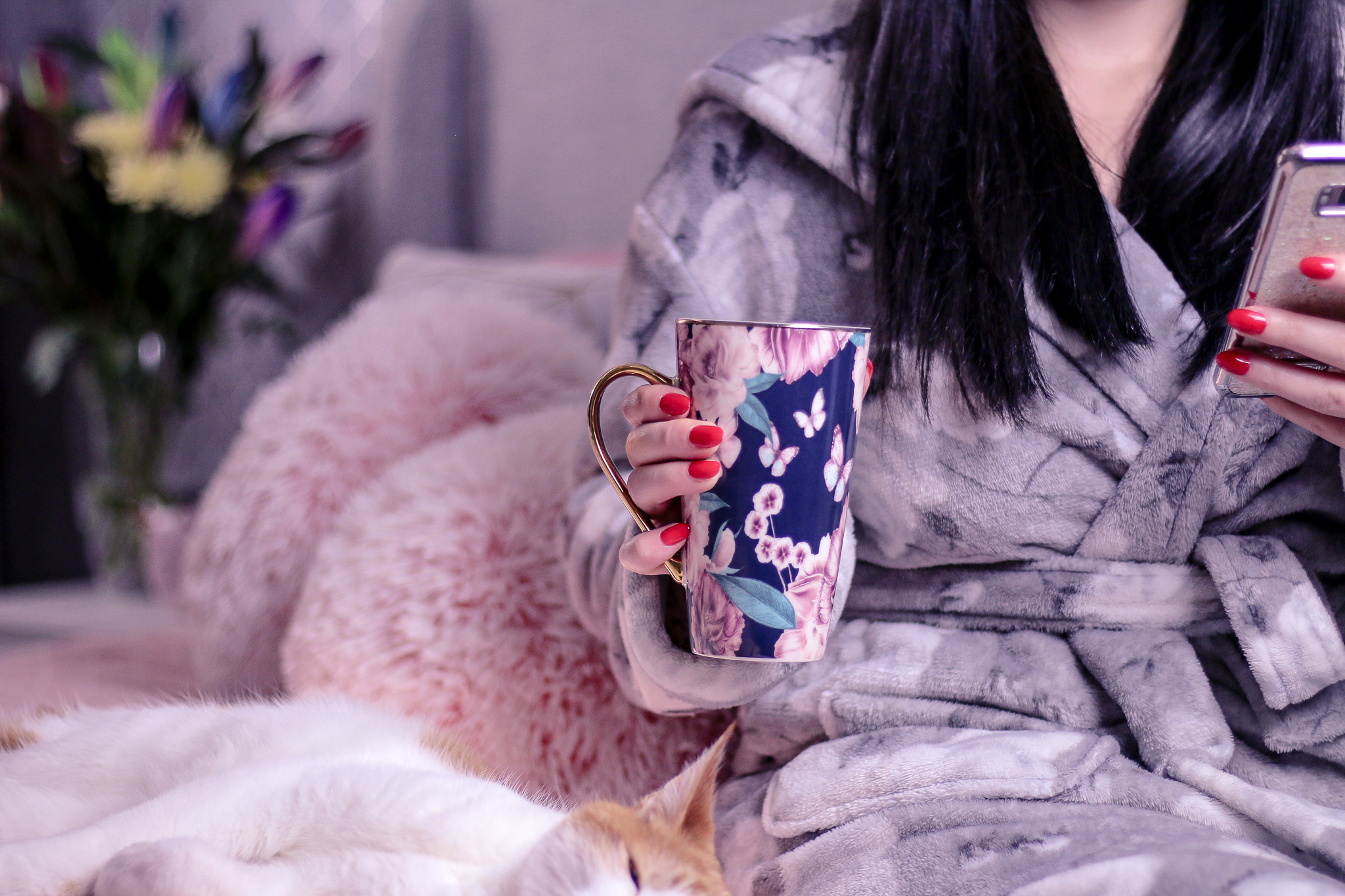 Photo of Jordanne from Thelifeofaglasgowgirl.co.uk Medium close up of Ofaglasgowgirl sitting on a bed that has pink bedding with her cat Ted to her right as she holds a flower mug