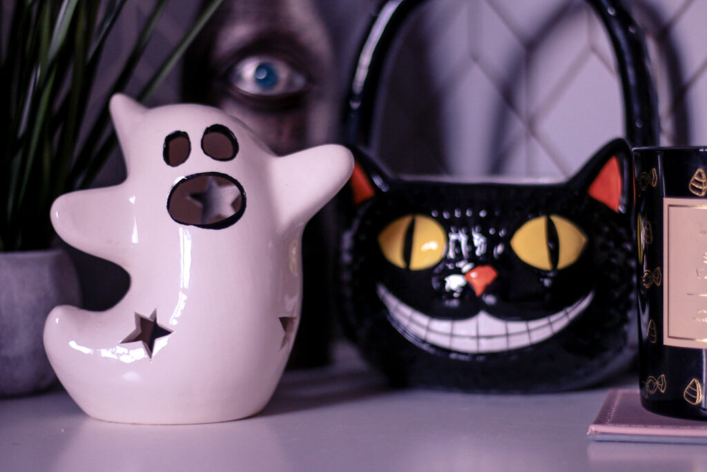 Close up photo of a white Ghost candle holder with a black cat basket in the background