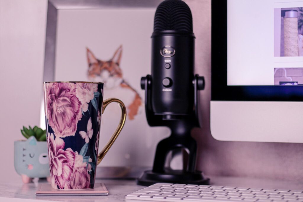 Close up of a flower mug on a white desk with a black blue yetti microphone and cat drawing behind it