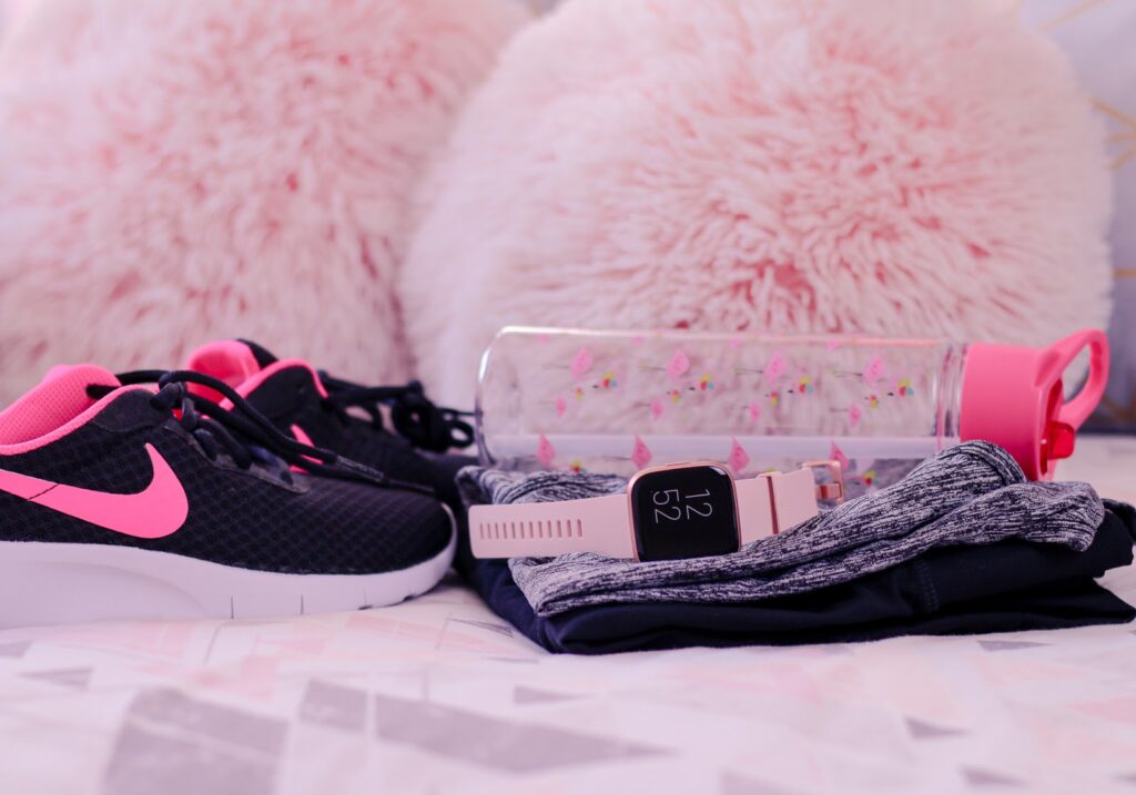 Close up photo of a fitbit versa 2, pink water bottle, nike trainers and work-out clothes on a bed