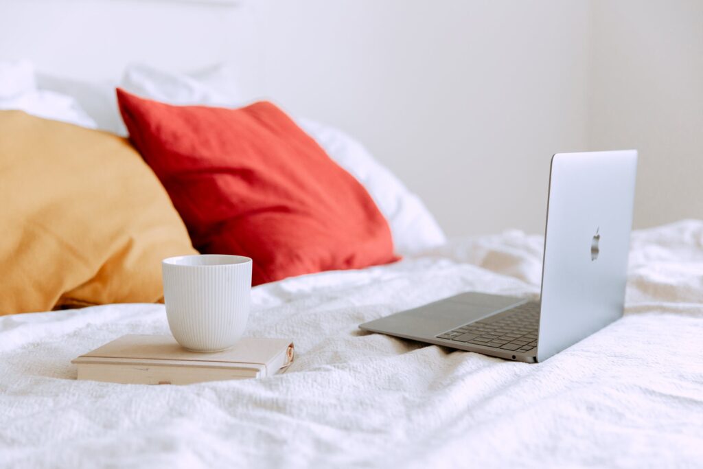 Stock photo from Pexels of a laptop on white bedding and a white mug next to it by Tatiana Syrikova