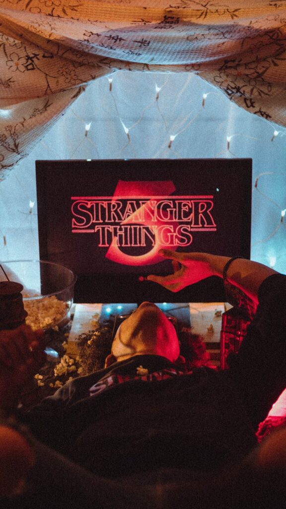 Stock photo from pexels by David Gomes of someone looking at a black TV which has the Stranger Things 3 Opening scene