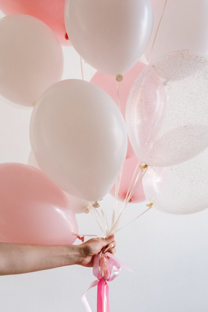 Stock photo from pexels by cottonbro of a person holding a bunch of pink and white balloons