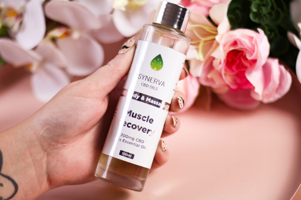 A close up photo of a woman holding a bottle of the Synerva CBD Oils body and massage oil muscle recovery.