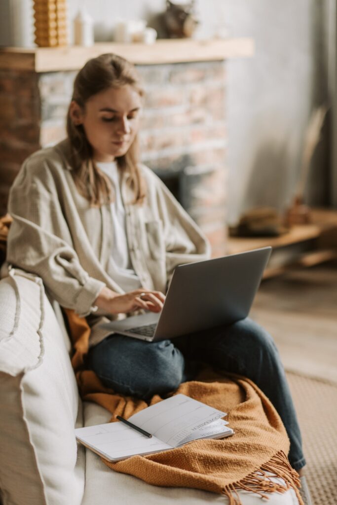 Stock photo from Pexels by Vlada Karpovich of a woman with blonde hair sitting on a couch wearing a grey shirt working on a silver laptop