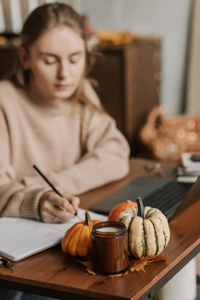 Stock photo from Pexels by Vlada Karpovich of a woman with blonde hair and a brown jumper writing in a note book 