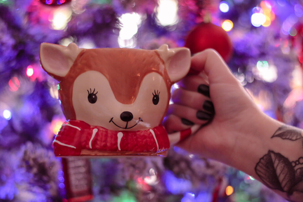 Close up photo of Jordanne holding a reindeer mug in front of a Christmas tree with blue lights.