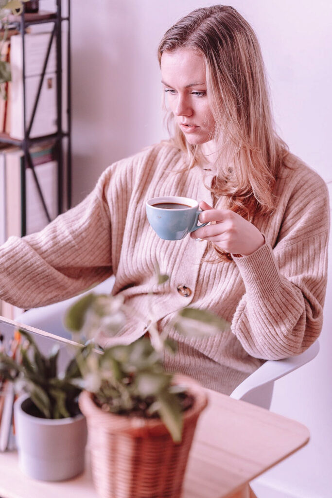 Stock photo from pexels by George Milton of a woman with blonde hair sitting with a blue mug in left hand and scrolling on laptop with right hand