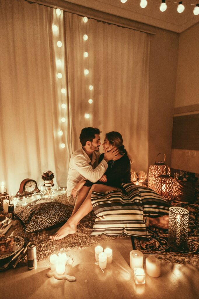 Stock photo from Pexels by Jonathan Borba of a couple sitting on a rug surrounded by pillows and candles as they hug and kiss for Valentine's Day
