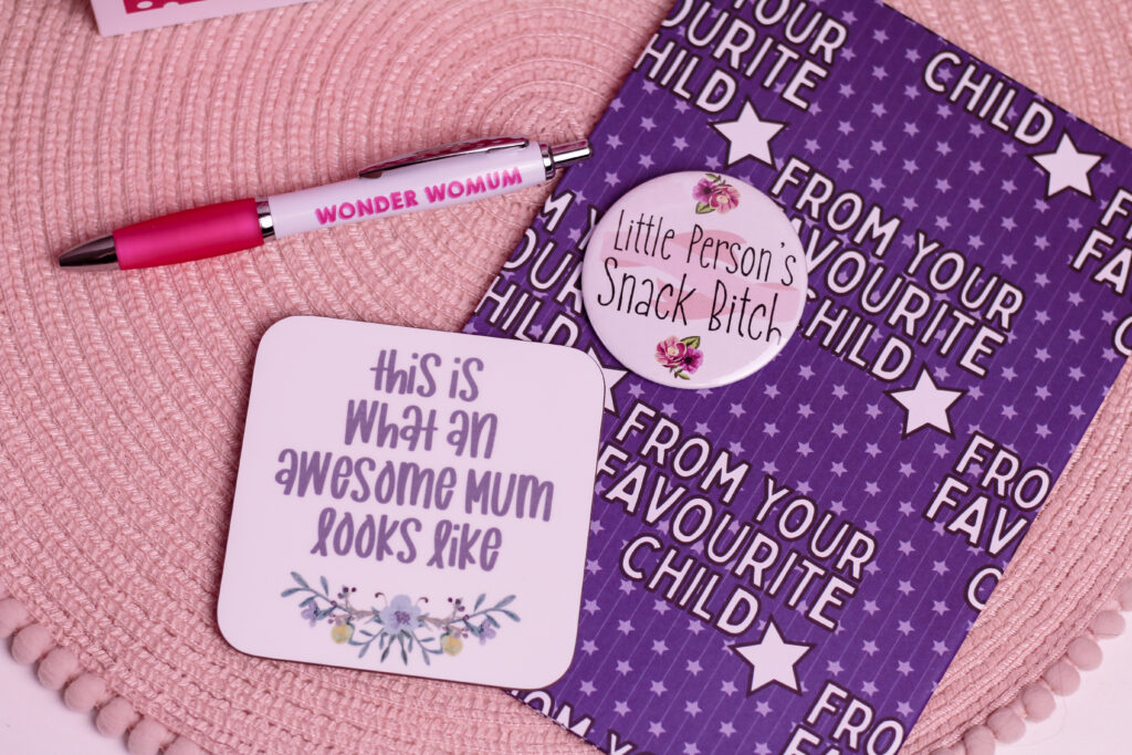 Birds eye view of some items from Love Layla including a pen, coaster, badge and wrapping paper that can be used in the Gift Basket Ideas for Mother's Day