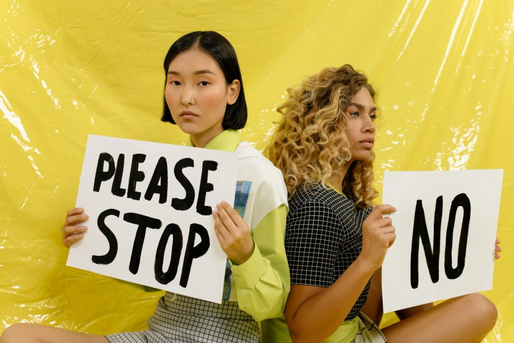 Stock photo from pexels by cottonbro of two women holding up cardboard signs that say "Please stop" and "no"