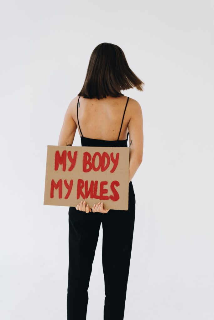 Stock photo from pexels by olia danilevich of a woman holding a cardboard sign that says "My Body, My Rules"