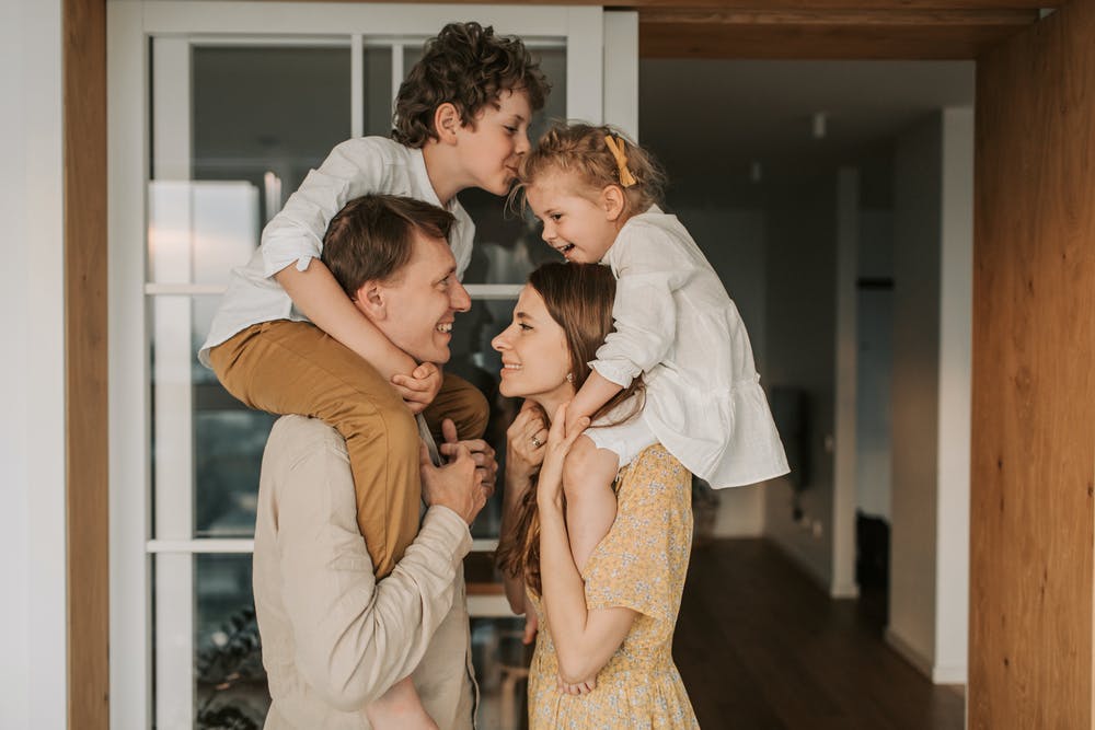 Stock photo from Pexels by Vlada Karpovich of Man in White Dress Shirt Kissing Woman in Brown Dress with children on their shoulders