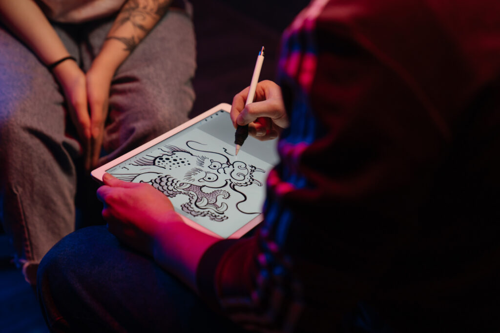 Stock photo from pexels by cottonbro of someone holding a white tablet and drawing a tattoo design