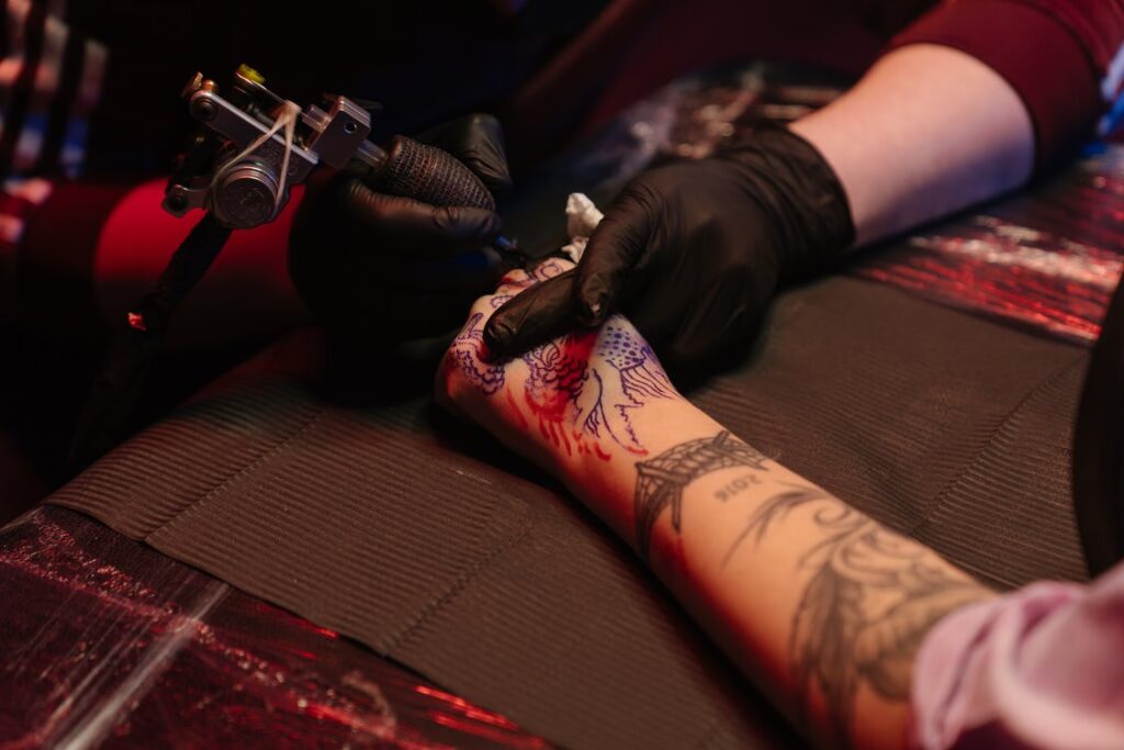 Stock photo from pexels by cottonbro of a man wearing black gloves holding a tattoo gun tattooing someone's hand