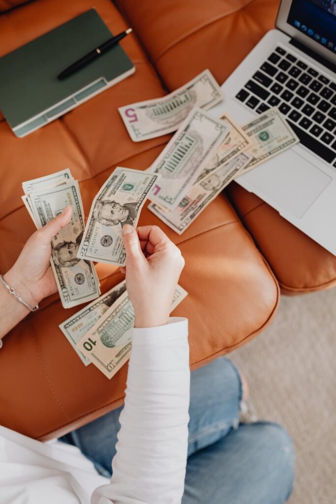 Stock Photo from Pexels by Karolina Grabowska of a woman setting money out on a couch with laptop to the side
