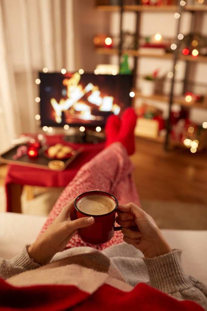 Stock photo from Canva of someone sitting with Christmas Pjs holding a mug of Hot Chocolate and Christmas lights in the background.
