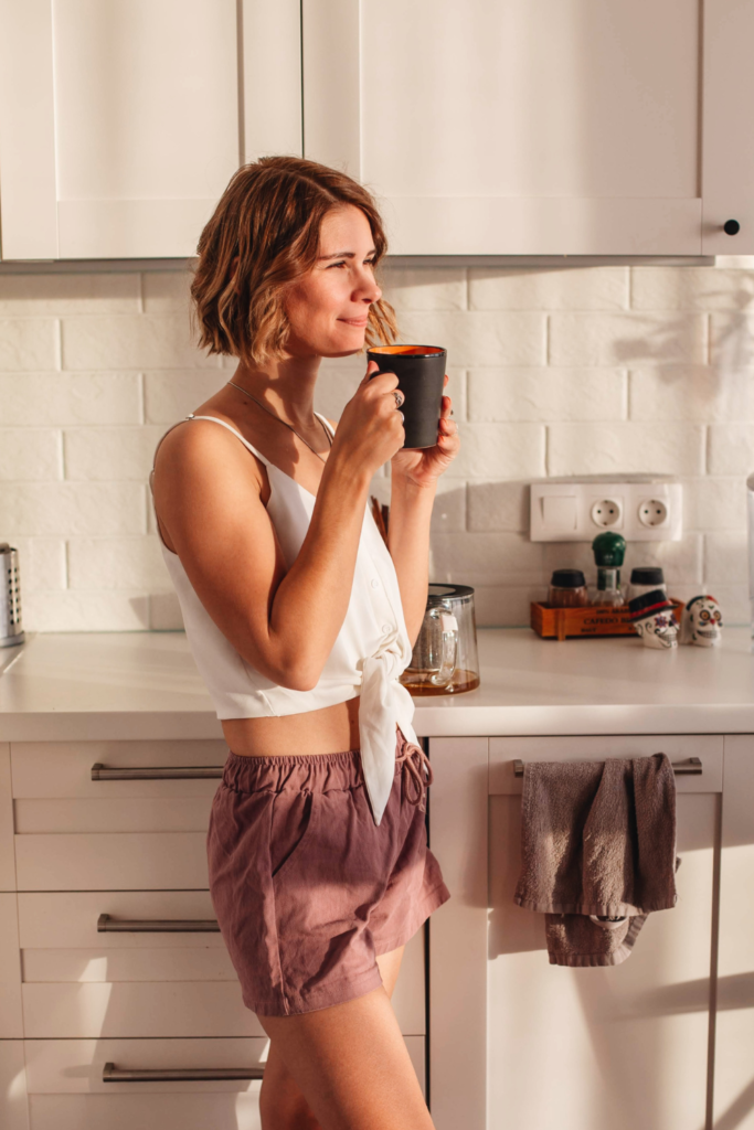 Stock photo from Pexels by Anna Alexes of a woman with short blonde hair in a beige kitchen smiling and holding a burgundy mug