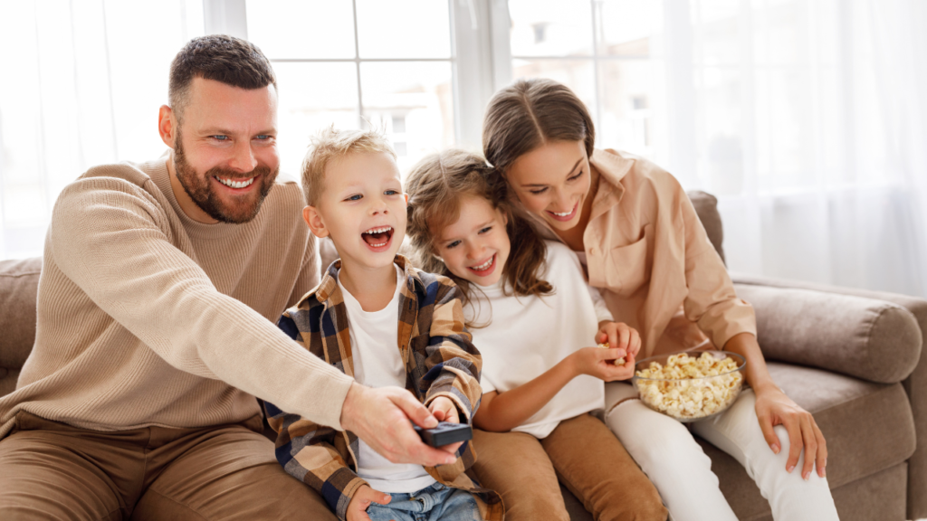 Stock photo from Canva of a family sitting on a couch laughing and watching television