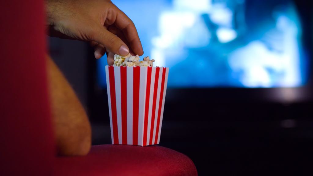 Stock photo from Canva of a hand reaching into a red and white stripe popcorn box