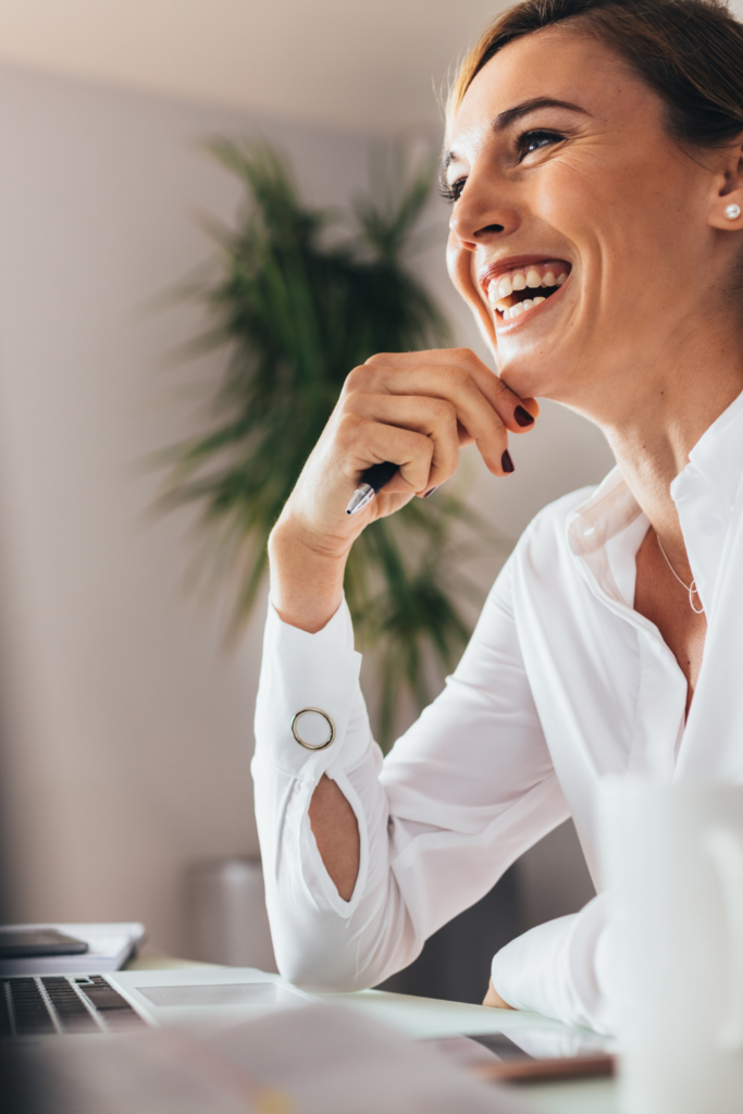 Stock photo from Canva by Jacob Lund of a woman smiling and sitting at a computer desk