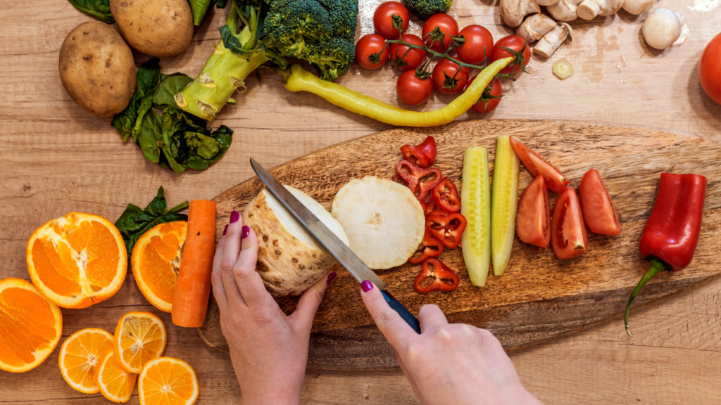 Stock photo from Canva by ljubaphoto at Getty Images of a person cutting vegetables on a wood chopping board