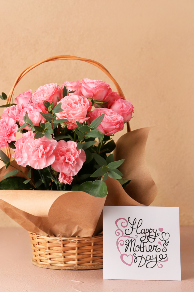 Stock photo from Canva by Pixelshot of a bouquet of pink carnations in a wicker basket with a Mother's Day card next to it