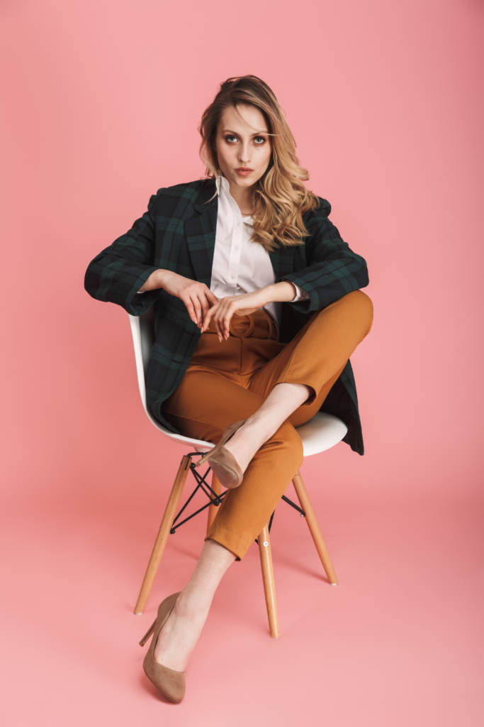 Stock photo from Canva by Dean Drobot of a business woman wearing make-up sitting on a chair with a pink background