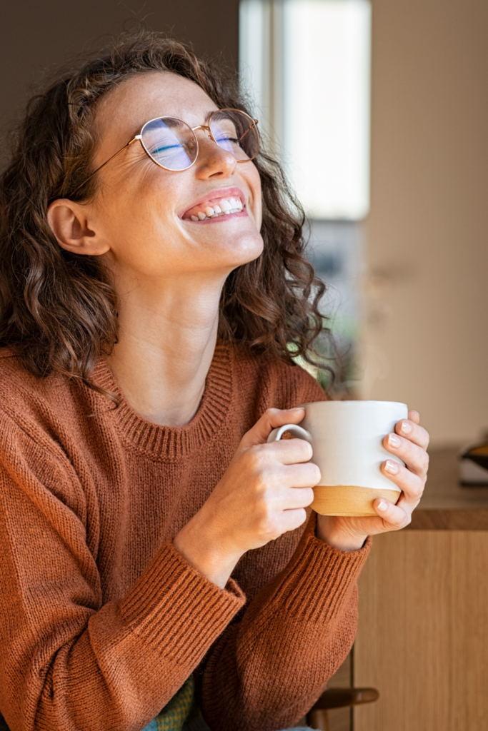 Stock photo from Canva by Rido of a woman with long brown hair and glasses holding a white mug smiling
