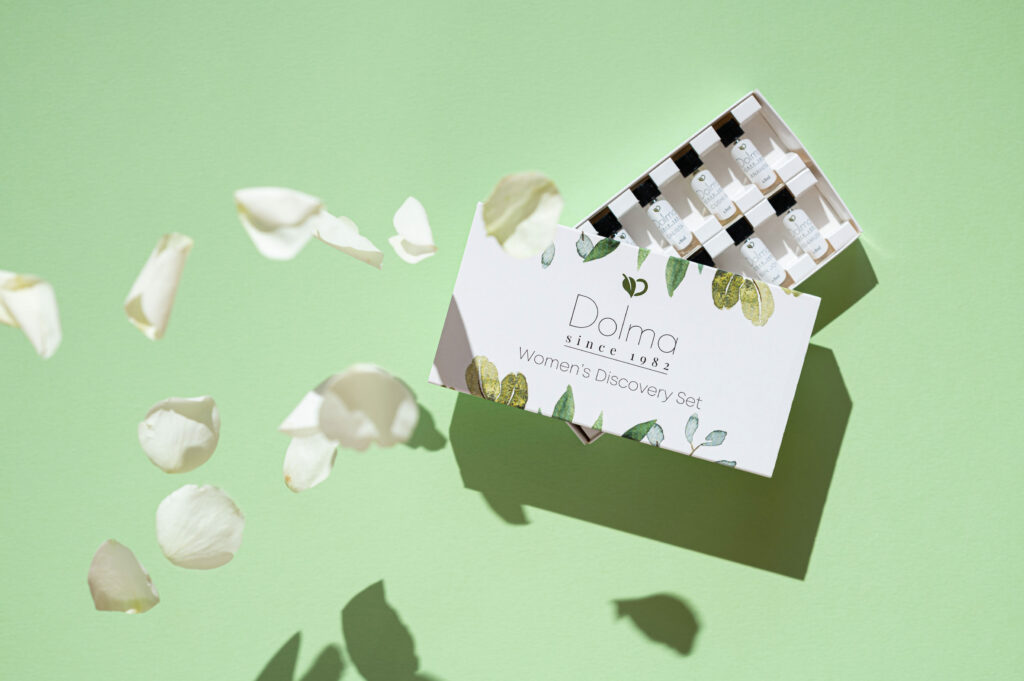 Birds eye view of Dolma Perfume Women's Discovery Set on a green background with white petals falling