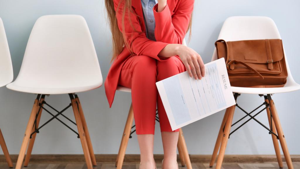 Stock photo from Canva by pixelshot of a woman sitting on a white chair holding a resume wearing a red suit