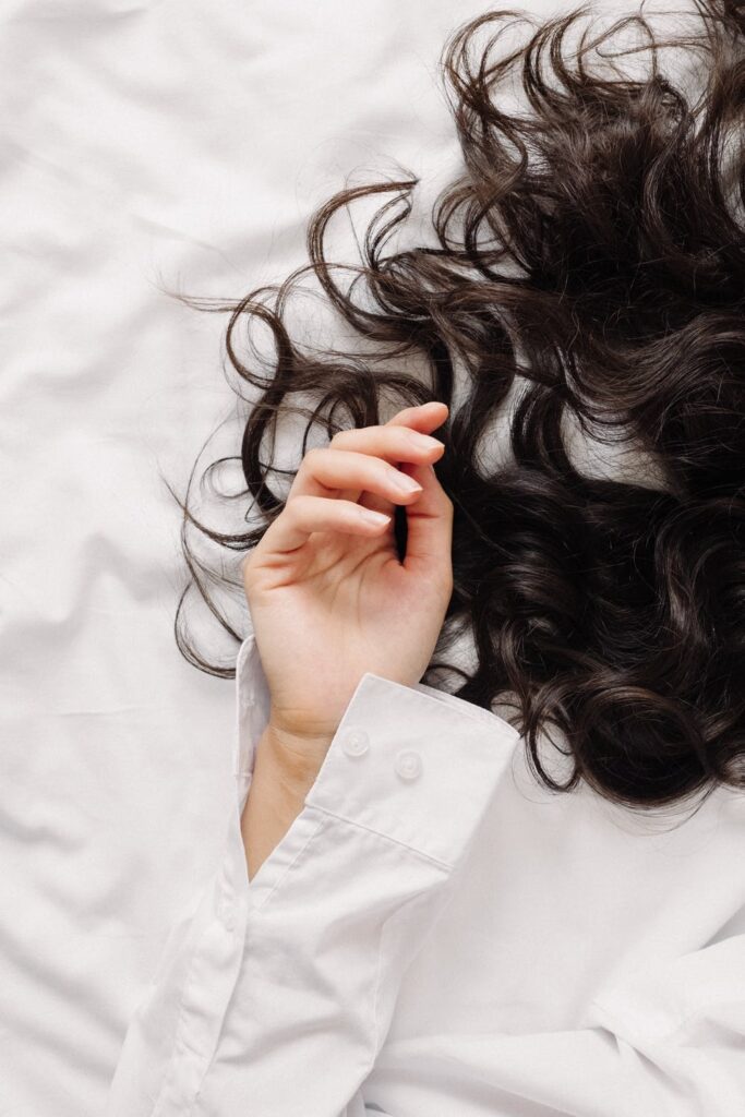 Stock photo from pexels by Ron Lach of a woman laying on a white sheet with long dark hair