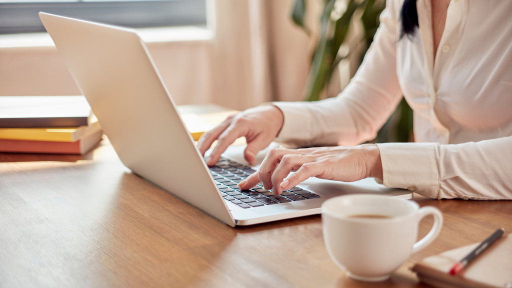 Stock photo from Canva by Hunur at Getty Images of a woman in a white shirt typing on a laptop